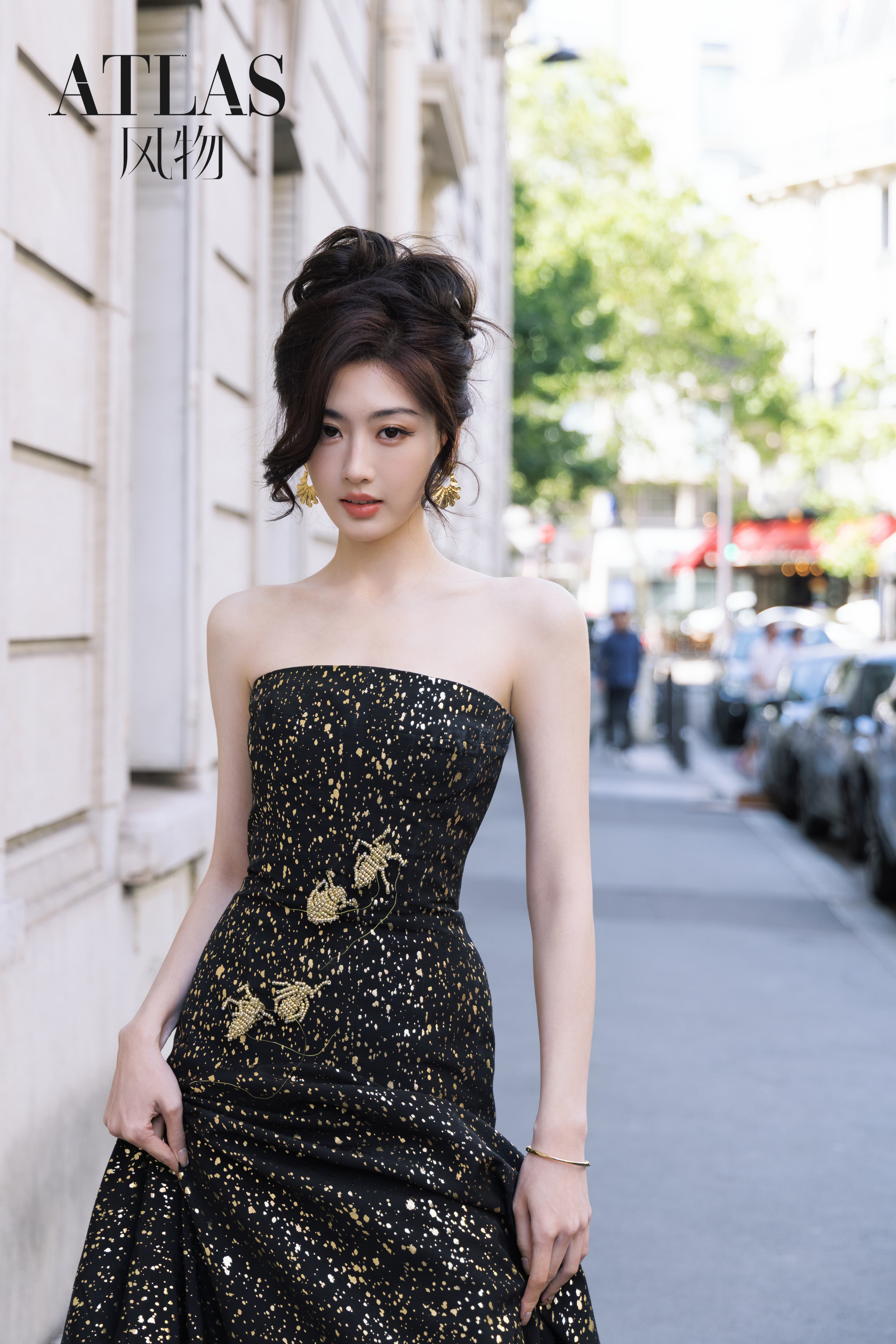 Sun Leyan facing the camera in a black-and-gold dress on a Paris street.