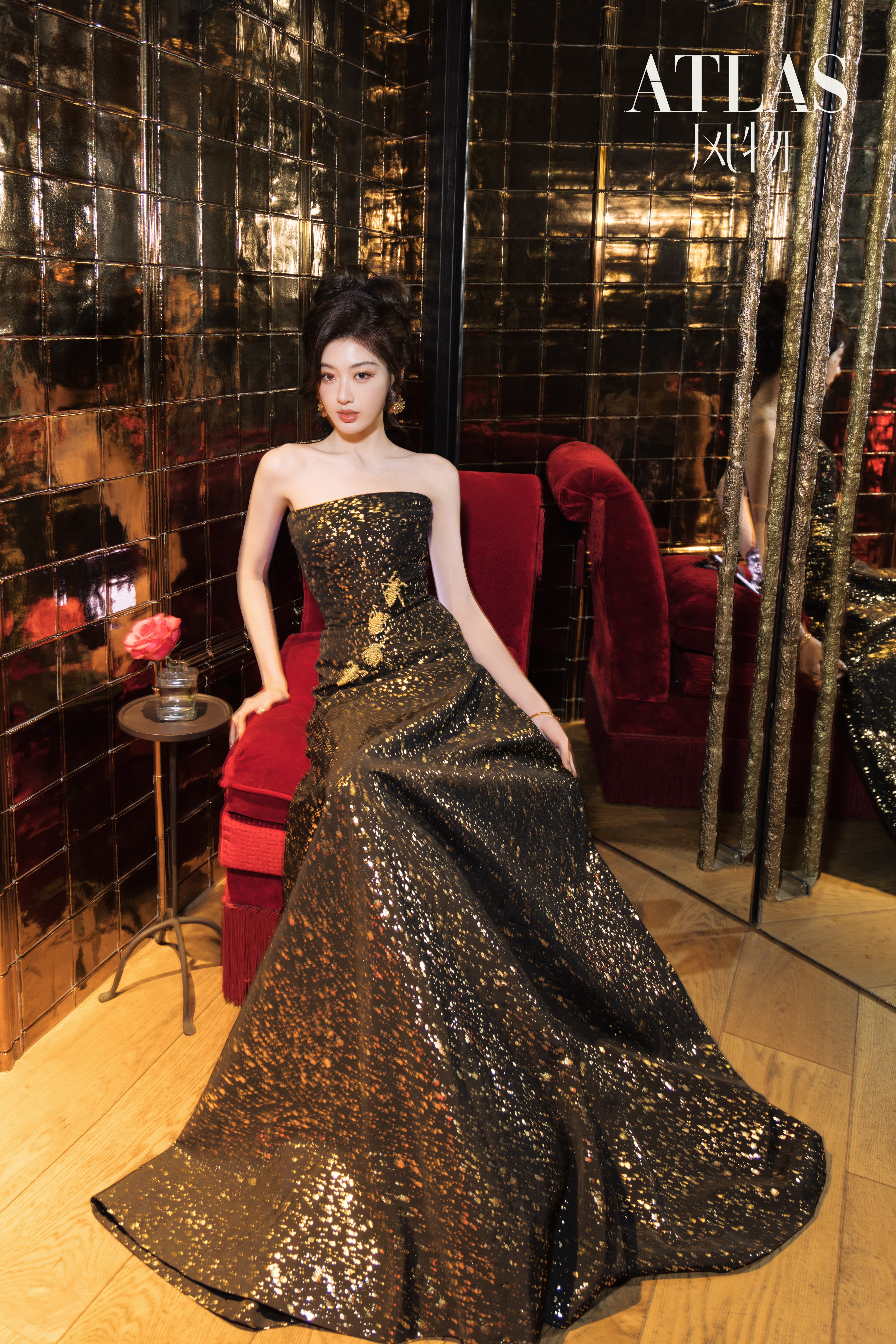Sun Leyan seated in a black-and-gold dress against red velvet and reflective walls.