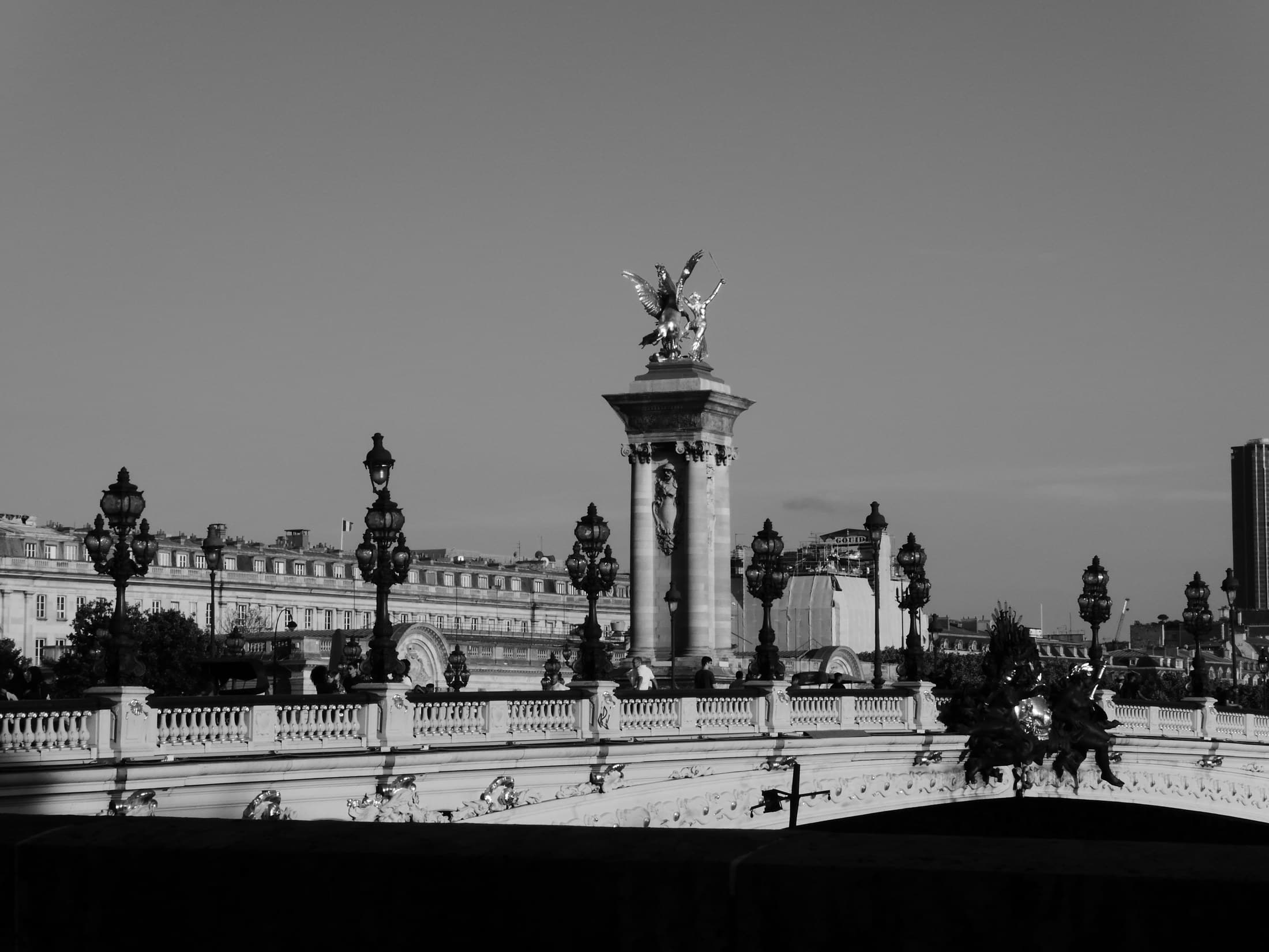 A black-and-white view of a Paris bridge and monumental column.