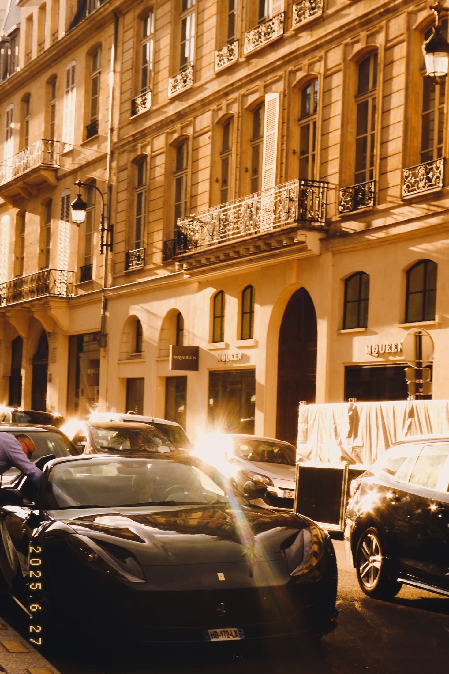 A warm Paris street at night with lit stone facade and passing cars.