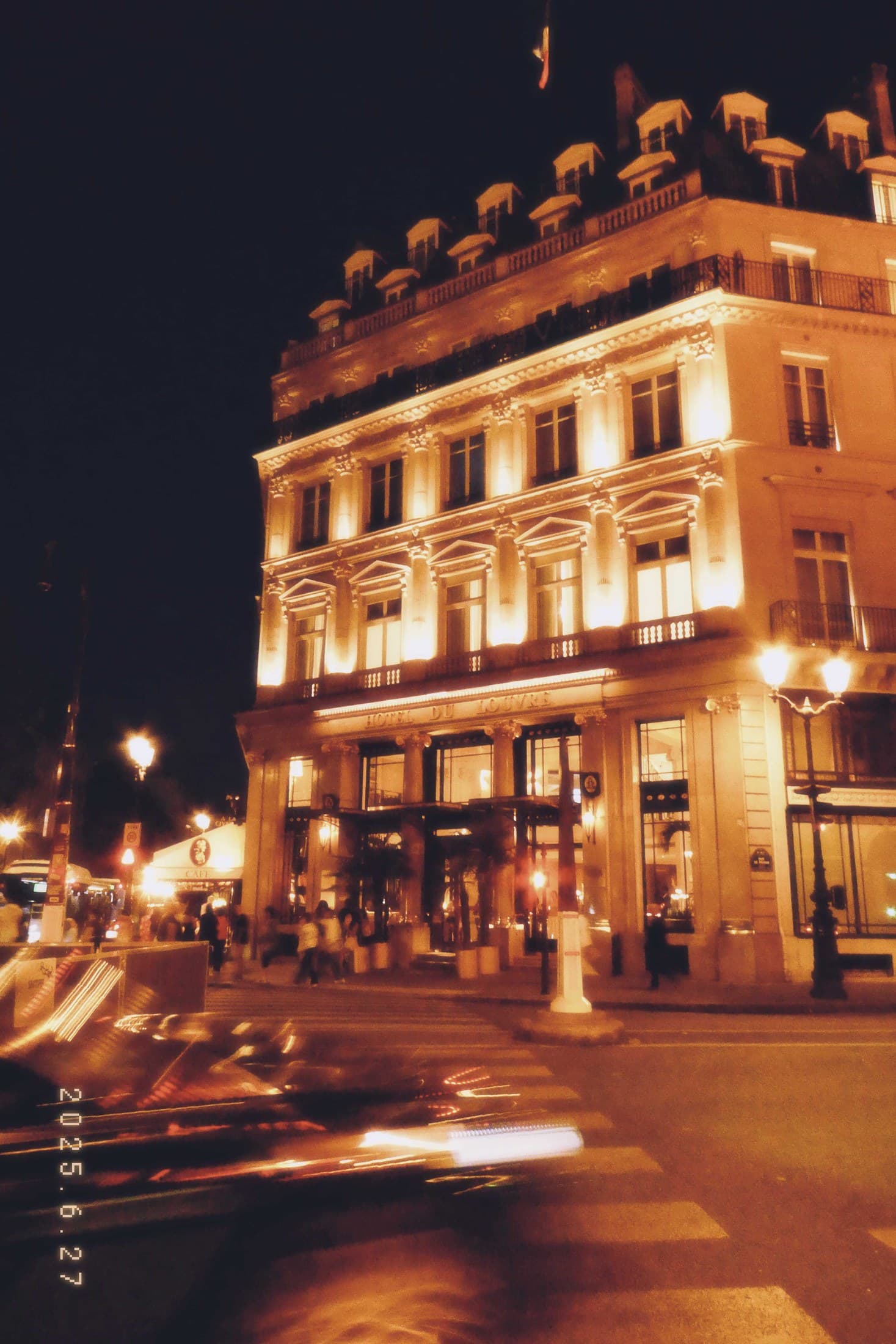 A warmly lit Paris corner building at night with blurred car lights.